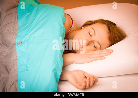 Woman lying on pillow in bed, covered with blue blanket Stock Photo
