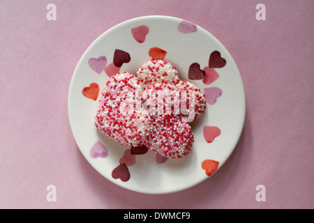 heart shaped shortcake biscuits decorated with vanilla flavour coating and red pink and white sugar pearls on heart plate - ideal for valentines day Stock Photo