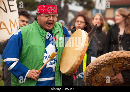 Aboriginal First nations man beating drum with demonstrators at Anti oil pipeline rally-Victoria, British Columbia, Canada. Stock Photo