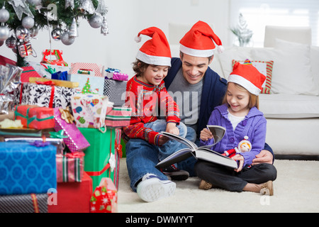 Siblings And Father Reading Book By Christmas Presents Stock Photo