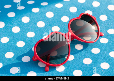 Red Heart shaped sunglasses on a blue polka dot table mat, 80s style sunglasses, vintage sunglasses accessory concept Stock Photo