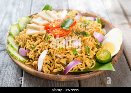 Malaysian style maggi goreng mamak or spicy fried curry instant noodles. Asian cuisine, ready to serve on wooden dining table setting. Fresh hot with steamed smoke. Stock Photo