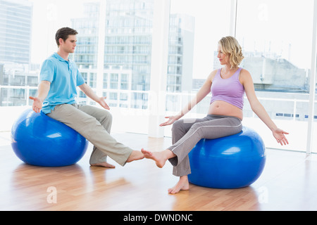 Trainer exercising with pregnant client on exercise balls Stock Photo