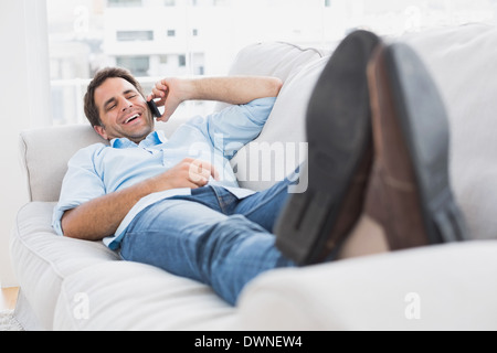 Happy man lying on the couch chatting on the phone Stock Photo