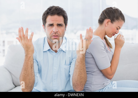 Man gesturing at camera with his crying partner on the couch Stock Photo