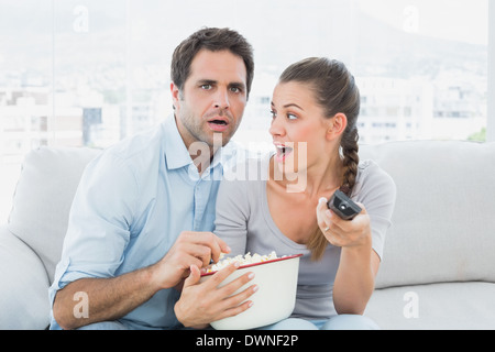 Couple watching scary movie on the couch with bowl of popcorn Stock Photo