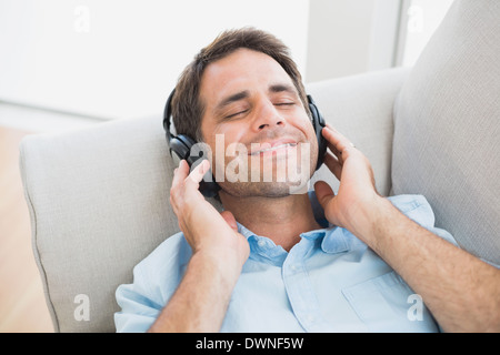 Smiling handsome man lying on sofa listening to music Stock Photo