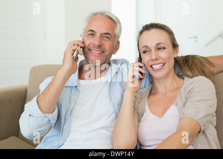 Happy couple sitting on couch talking on their phones Stock Photo