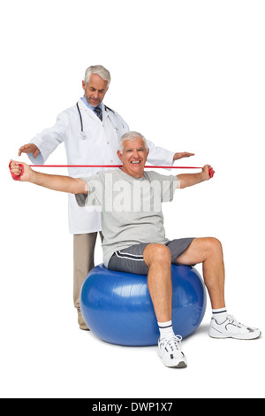 Mhysiotherapist looking at senior man sit on exercise ball with yoga belt Stock Photo