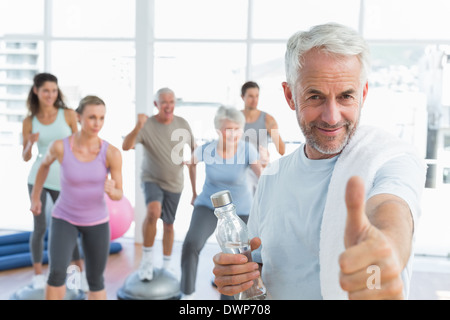 Senior man gesturing thumbs up with people exercising in fitness studio Stock Photo