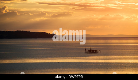 Tranquil summer night scene in Sweden. Silhouette of small steamboat on lake Vattern at sunset. Stock Photo