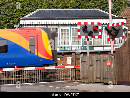Train passing Petersfield 1880's Type 3 Signal Box with down full barrier type level crossing. Stock Photo