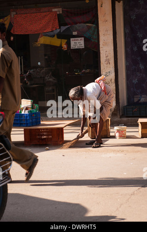 South Southern India Tamil Nadu Madurai street scene stooped old lady woman female sweeps road with twig brush broom Stock Photo