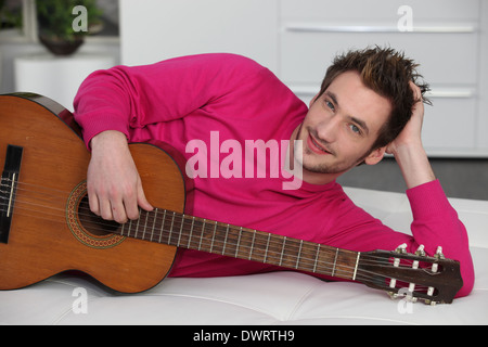 Man laying on sofa with acoustic guitar Stock Photo