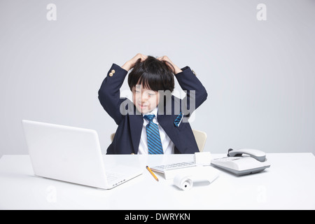 a kid wearing a business suit looking stressed while using computer Stock Photo