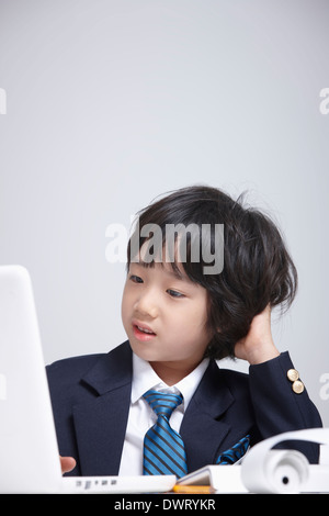 a kid wearing a business suit looking stressed while using computer Stock Photo