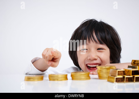 a kid wearing a business suit with coins and gold bars Stock Photo