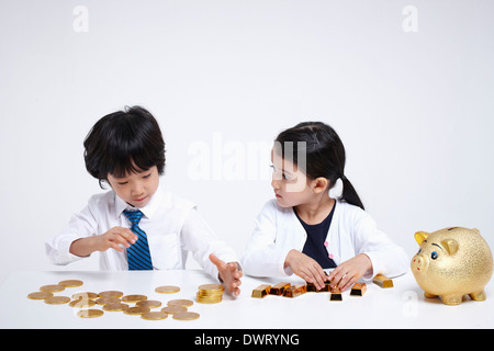 kids wearing business clothes at a table with coins and gold bars Stock Photo