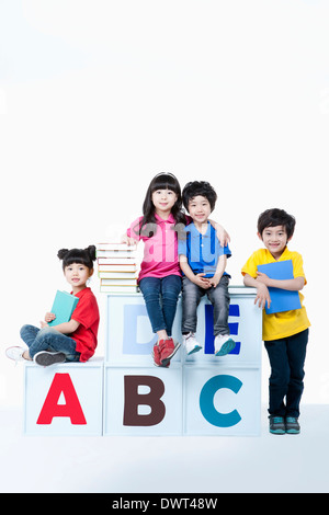 kids standing and sitting around alphabet blocks with books Stock Photo