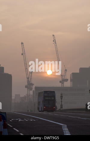 LONDON, UK, 13th Mar, 2014. London starts the day swathed in a blanket of fog. The sun rises behind cranes near St Thomas' Hospital, Westminster as a London bus crosses Westminster Bridge Credit:  Steve Bright/Alamy Live News Stock Photo