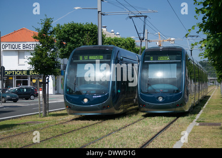 Two public transportation Tramway trains using overhead wires in Bordeaux France pass on grass covered rails. Stock Photo