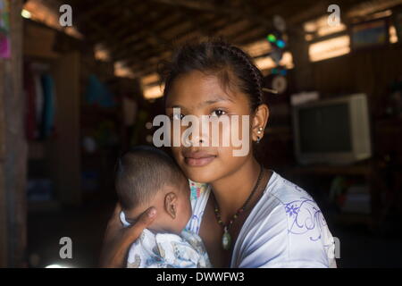 Mar 2, 2014 - Ko Surin, Thailand - Dian, a 17 year old Moken woman, and her baby in their home in Ko Surin National Park. Often called sea nomads or sea gypsies, the Moken are a seafaring people who for centuries lived nomadically on the Andaman Sea. However, due to stricter border control, commercial overfishing, rapid development, and tourism, the Moken have gradually been forced to adopt a settled lifestyle. Today, the Moken who live in Koh Surin National Park, one of Thailand's most remote group of islands, have it better than many of their kin and are still able to live a lifestyle largel Stock Photo