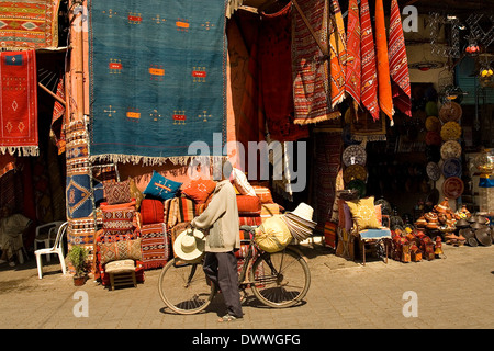 Man selling hats with his bicycle outside a carpet shop in a souq in Marrakech, Morocco Stock Photo