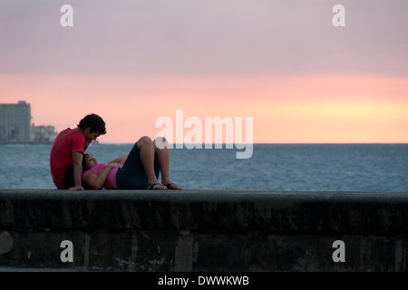 Couple relaxing on the wall of the Malecón at sunset in Centro Habana, Havana, Cuba Stock Photo