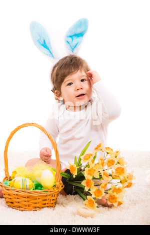 Ester bunny baby with basket with eggs and flowers sitting on carpet Stock Photo