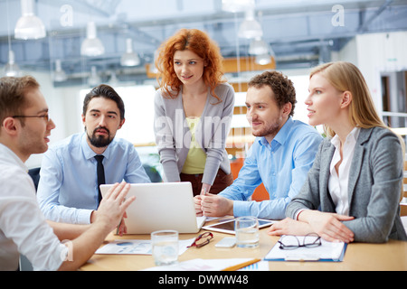 Group of business partners looking at young man presenting computer project at meeting Stock Photo