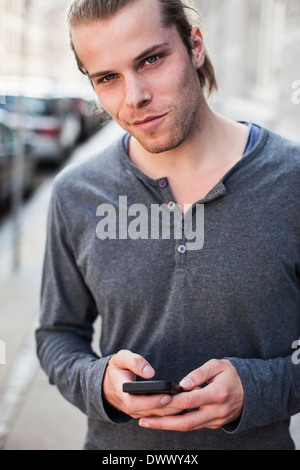 Portrait of young man holding mobile phone outdoors Stock Photo