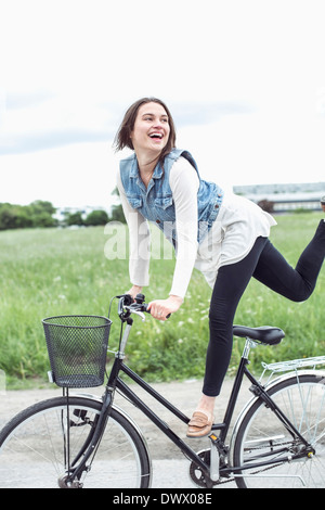 Happy young woman performing trick on bicycle at countryside Stock Photo
