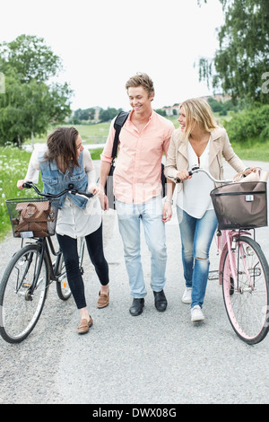 Happy young friends with bicycles walking on country road Stock Photo