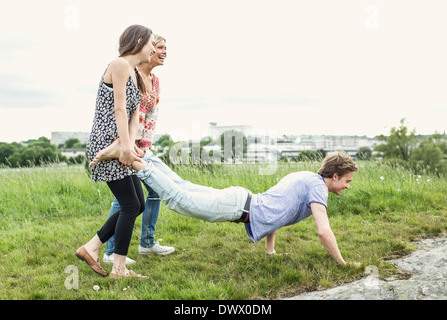 Happy young women holding male friends legs doing push-ups on field Stock Photo