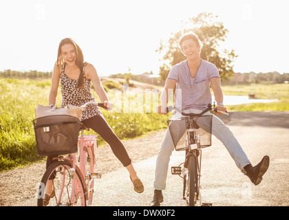 Portrait of happy young couple with legs apart cycling on country road Stock Photo