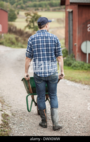 Farmer walking and pushing a wheelbarrow full of gold plates isolated ...