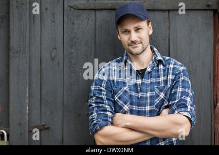 Portrait of confident farmer standing arms crossed against barn door Stock Photo