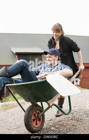 Woman pushing man in wheelbarrow on rural road Stock Photo