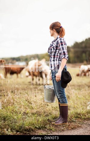 Female farmer with bucket standing on field with animals grazing in background Stock Photo