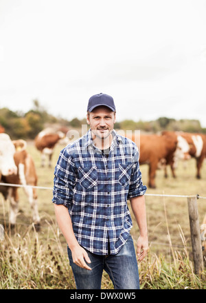 Portrait of confident farmer standing on field while animals grazing in background Stock Photo