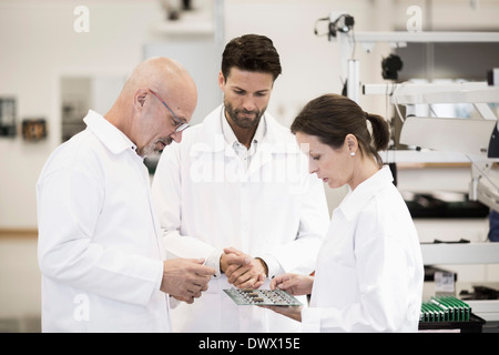 Team of technicians examining circuit board in factory Stock Photo