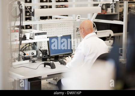 Rear view of mature engineer using computer in manufacturing plant Stock Photo