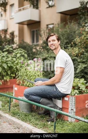 Full length portrait of young man with gardening equipment sitting in garden Stock Photo