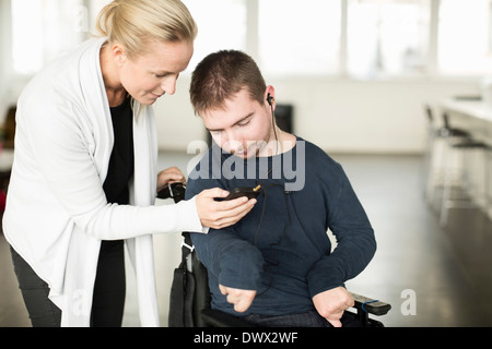 Female caretaker assisting disabled man in using mobile phone at home Stock Photo