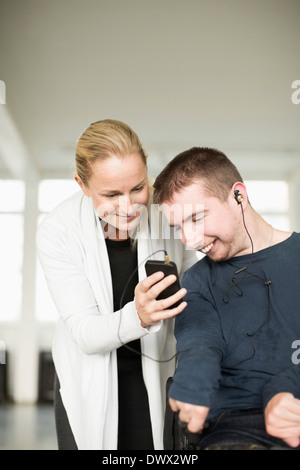 Female caretaker assisting disabled man in using mobile phone at home Stock Photo