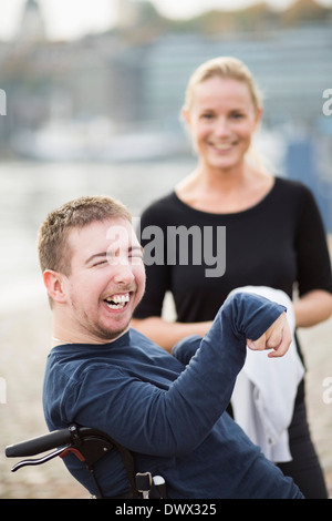 Disabled man on wheelchair laughing by caretaker outdoors Stock Photo