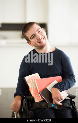 Disabled man with books sitting on wheelchair at home Stock Photo
