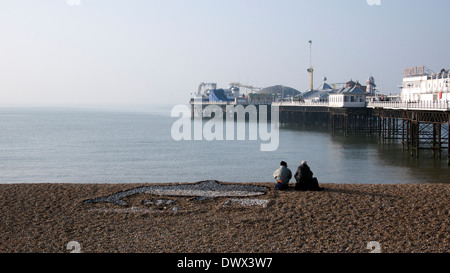 Two people sitting on beach, brighton pier,looking out to sea Stock Photo