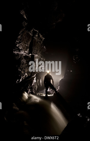 A caver in silhouette in the stream passage in Ogof Ffynnon Ddu, Brecon Beacons, south Wales Stock Photo