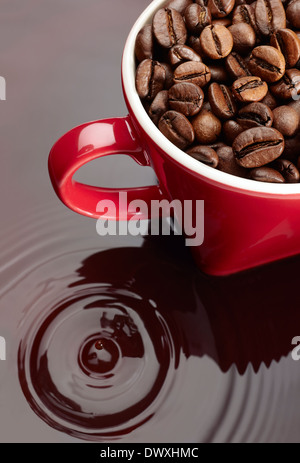 Natural coffee beans on a red mug on reflected background. Stock Photo